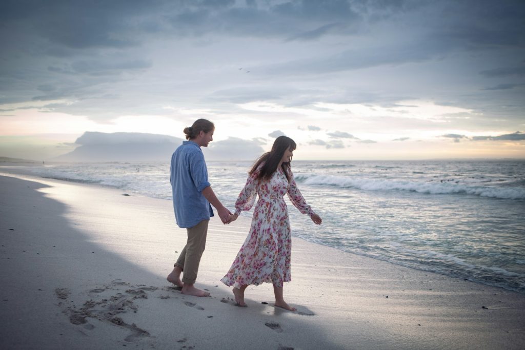 Pareja caminando tomados de la mano por una playa de la Costa Brava en su aniversario